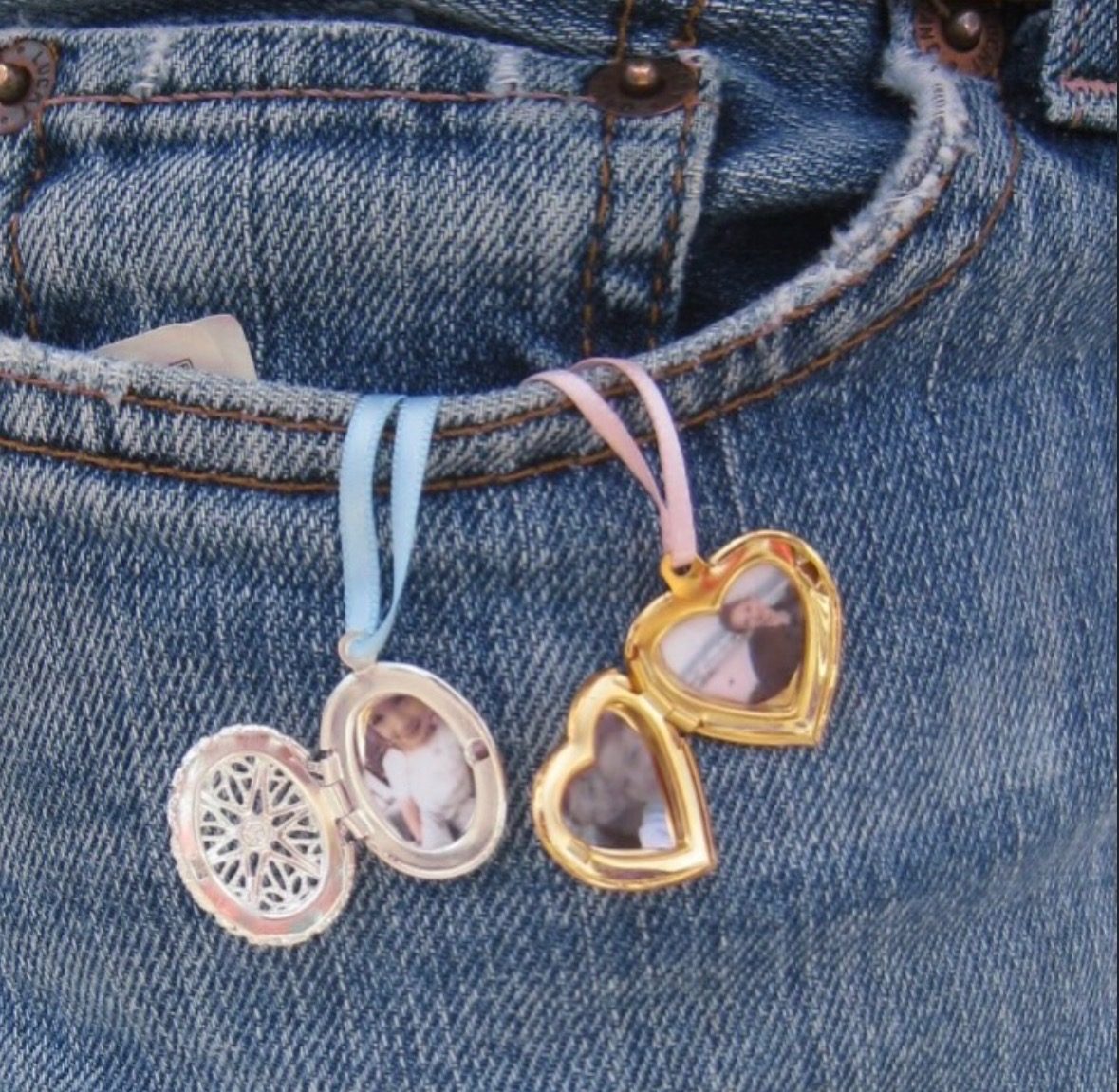 Two open lockets on ribbon tucked into a jeans pocket